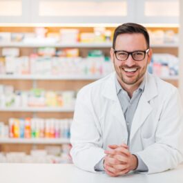 male-pharmacist-smiling-desk-shelving