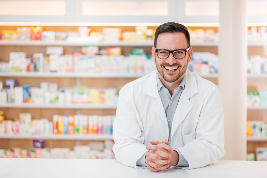 male-pharmacist-smiling-desk-shelving